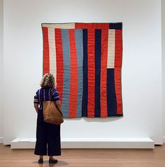 a woman standing in front of a quilt hanging on the wall with her back to the camera