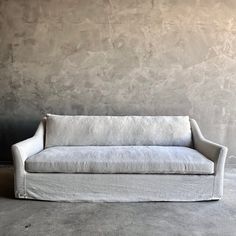 a white couch sitting in front of a wall with a concrete floor and walls behind it