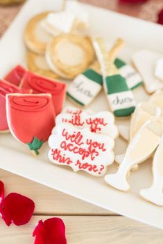 decorated cookies on a tray with rose petals and wine corks in the background that says, will you accept this note?