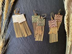 three pairs of earrings hanging from hooks on a black surface next to some wheat stalks