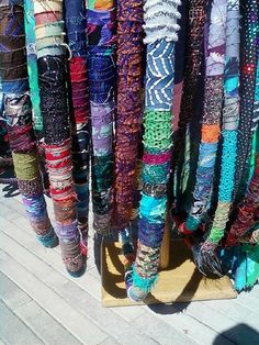 there are many different colored scarves hanging from the rack together on the boardwalk at the beach