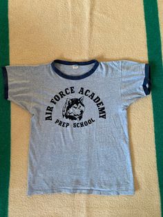 A Vintage Champion Blue Bar Ringer t shirt. US Air Force Prep School graphic with Husky mascot. Made in USA, cotton blend. A few holes, shown in photos. Previous owners name written on the inside of the hem. Collar is a little loose. Size marked large but please refer to the actual measurements: 19 inches from pit to pit measured lying flat, 19 inches across the shoulders and the overall length is 25 inches. Cotton T-shirt With Letter Print For Fan Conventions, Retro Crew Neck T-shirt For School, Retro Cotton T-shirt For Fan Gear, Band Merch Cotton T-shirt For Fans, Blue Crew Neck Tops For Fan Conventions, School Crew Neck T-shirt With Logo Print, Cotton T-shirt With Text Print For Fan Conventions, Blue Cotton Tops For Fan Conventions, Band Merch Cotton Tops For Fan Conventions