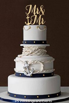 a white and blue wedding cake with an anchor on the top is decorated with gold lettering