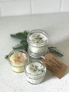 three small candles sitting on top of a counter next to pine cones and evergreen branches