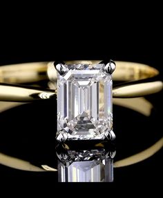 an emerald - cut diamond sits on top of a black surface, surrounded by two gold rings