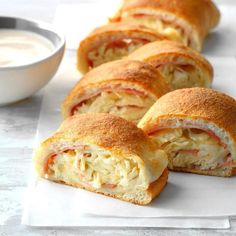 several rolls with meat and cheese are on a white plate next to a bowl of ranch dressing