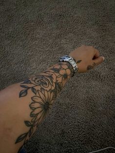 a person's arm with a flower tattoo on it and a cell phone in the other hand