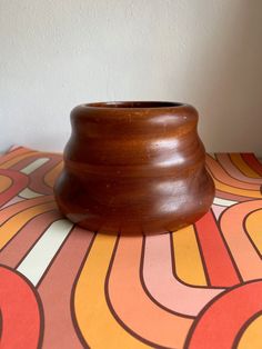 a wooden vase sitting on top of a colorful table cloth with an abstract design in the background