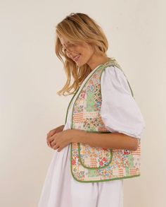 a woman wearing a white dress and carrying a colorful handbag with flowers on it