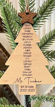 a wooden christmas tree ornament hanging from a pine tree with names on it