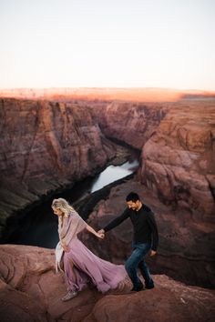 a man and woman holding hands while standing on top of a cliff