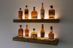 several bottles of liquor are lined up on wooden shelves in front of a white wall