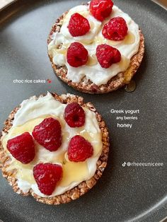 two desserts with raspberries and cream on top are sitting on a black plate