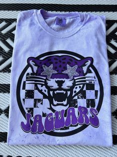 New product- Preppy Jaguars Mascot Shirt! Each shirt is meticulously printed by me using high-quality materials on a Comfort Colors shirt, known for its exceptional comfort and durability. Whether you're cheering on the Jaguars at the stadium or simply want to showcase your school spirit in your everyday attire, this shirt is the perfect choice. Available in Unisex sizes S to 3X, we've got you covered regardless of your preferred fit. The Preppy Jaguars Shirt features a classic crew neck and short sleeves with a fun splatter print! This preppy Jaguars shirt is a definite conversation starter and a unique fashion statement- wear it with jeans, shorts, or leggings for a casual and trendy look that showcases your Jags spirit! Note: As each shirt is individually printed, slight variations in c Cheap Shirt With Funny Print For School Spirit, Purple School Spirit T-shirt With Graphic Print, Purple Cotton Shirt With Custom Print, Purple Cotton Shirt With Sublimation Print, Purple Cotton Top With Sublimation Print, Cotton Purple Top With Sublimation Print, School Spirit Cotton Shirt With Graphic Print, School Spirit Shirt With Graphic Print For Fans, Cotton School Spirit Shirt With Graphic Print