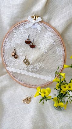 a vase with yellow flowers and earrings in it next to a white lace doily