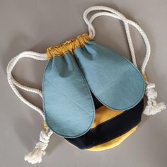 a blue and yellow handbag hanging from a white string on a gray wall with two tassels attached to it