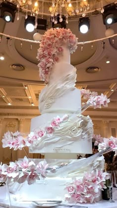 a large white wedding cake with pink flowers on the top and bottom tier is surrounded by chandeliers