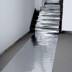 an empty hallway with water running down the floor and on the ground, in front of a white wall