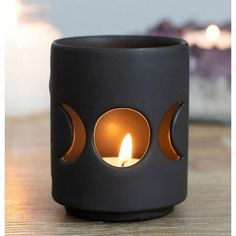 a black candle holder sitting on top of a wooden table with a lit candle in the middle