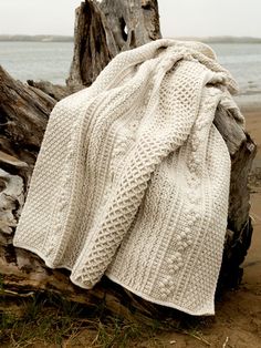 a white knitted blanket sitting on top of a tree stump next to the ocean