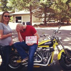 a man sitting on the back of a motorcycle next to a woman holding a for sale sign