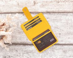 a yellow card case sitting next to a dried flower on a wooden table with white wood planks