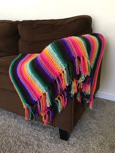 a multicolored blanket draped over a brown couch in a room with carpeting