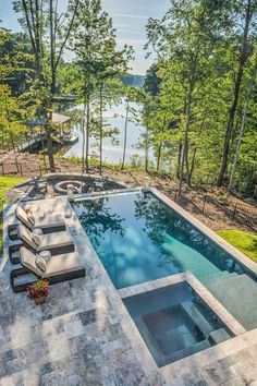 an outdoor swimming pool surrounded by trees and water with lounge chairs around the edge in front of it