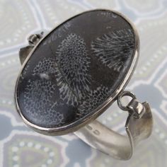 A large unique cabochon of coral from the Madura Island region (off coast of East Java) is set in this vintage Bali sterling silver bracelet.  The large 51mm x 34mm oval coral piece is of brown color with black to grey striations and round shapes. There are fissures to the coral that go across it, as pictured. The coral feels very smooth and very sturdy in its setting. The thick bezel is connected to a 1/2 inch wide curvy cuff form. One side has a hook closure. The inside is signed with a fish s Unique Cabochon Cuff Bangle Bracelet, Unique Cabochon Bangle Bracelets, Unique Silver Bracelet With Cabochon, Silver Cuff Bracelet With Cabochon, Unique Silver Cuff Bracelet With Cabochon, Sterling Silver Oval Cuff Bracelet, Unique Handmade Oval Cuff Bracelet, Unique Oval Cuff Bracelet Collectible, Glass Store