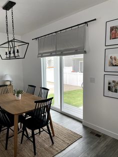 a dining room table with black chairs next to a sliding glass door and pictures on the wall