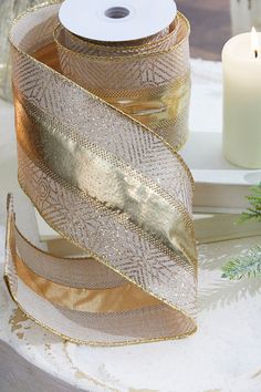 two rolls of gold ribbon sitting on top of a table next to a lit candle