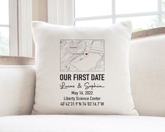 a white pillow sitting on top of a couch next to a window with the words our first date printed on it