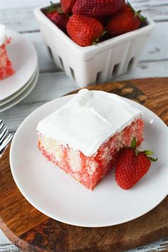 a piece of strawberry cake with white frosting and strawberries on the plate next to it