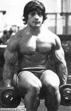 a man sitting on top of a bench holding two dumbbells