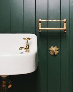 a white sink sitting next to a green wall with a gold faucet on it