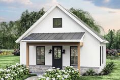 a small white house with a black door and windows on the front porch is surrounded by flowers