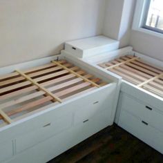 two white beds with wooden slats in a room next to a window and wood flooring