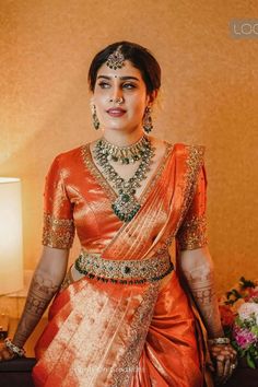 a woman in an orange and gold sari standing next to a table with flowers