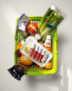 a green shopping basket filled with vegetables and condiments on top of it's side