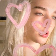 a woman with long blonde hair is looking at the camera and has pink hearts drawn on her face