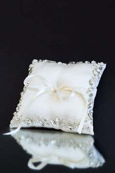 a white ring pillow with a bow on the front and ribbon at the back, sitting on a reflective surface