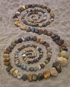 two spirals made out of rocks in the sand with one being surrounded by smaller rocks