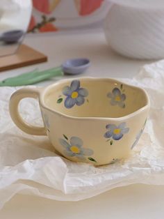 a blue and yellow flowered cup sitting on top of a white table cloth next to scissors