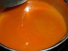 an orange liquid in a metal bowl with a spoon