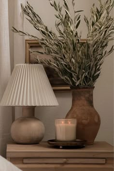 a table with a vase and candle on it next to a lamp shade that is turned on