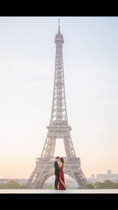 an engaged couple standing in front of the eiffel tower