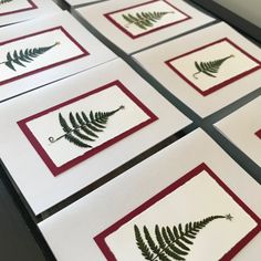 four cards with green leaves on them sitting on a table next to each other in red and white frames