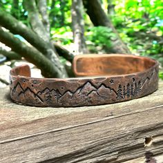 This handmade copper bracelet features stamped images of mountains and trees, with the moon and stars, which celebrate the natural beauty and majesty of the forest. It is ideal for outdoor enthusiasts such as hikers and hunters. Each piece is unique due to the hand-forged process and hammered finish that gives the bracelet a rustic appearance. Please note that color variations may occur due to differences in viewing screens. To ensure the perfect fit, follow the instructions in the accompanying Adjustable Nature-inspired Jewelry For Outdoor, Adjustable Nature-inspired Outdoor Jewelry, Handmade Copper Bracelet, Mountains And Trees, Metal Ideas, Hammered Bracelet, The Moon And Stars, Copper Wire Jewelry, Copper Cuff Bracelet