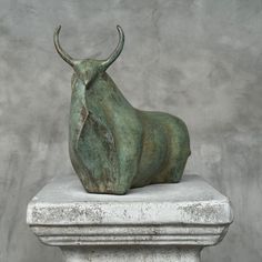 an animal statue sitting on top of a white marble pedestal in front of a gray wall