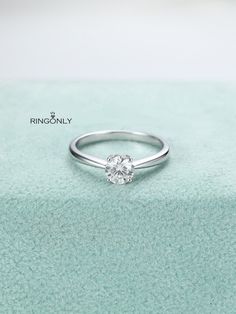 a white diamond ring sitting on top of a green velvet covered surface with a light blue background